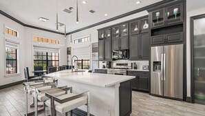 A spacious kitchen with a large island, dark cabinets, stainless steel appliances, and a view to the outdoors. - Homestead Highlands: Pool, Game Room, Theater, Themed, Water Park, Near Disney (Kissimmee)