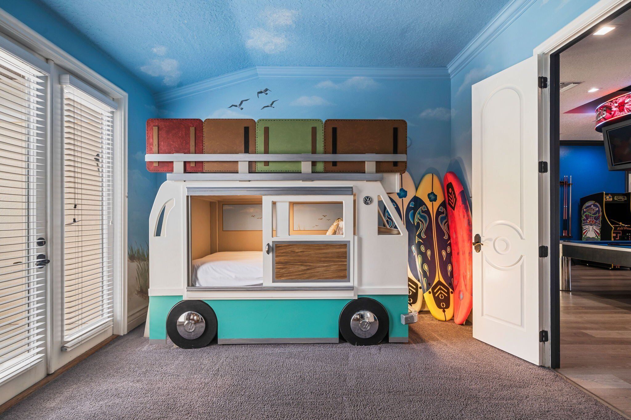 Ein Kinderstockbett im Camping-Design, in einem Raum mit blauer Decke und Surfbrettern an der Wand.