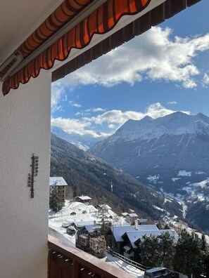A mountain view from a balcony with a red awning, snow-covered houses, and a clear sky.