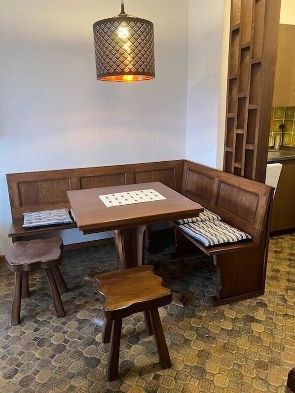 A corner dining area with a wooden table and bench seating, a patterned floor, and a hanging light fixture.