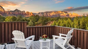 A deck with two white Adirondack chairs and a small table with a vase of flowers, overlooking a mountainous landscape. - Sedona Red Rock Serenity Retreat! (Sedona)