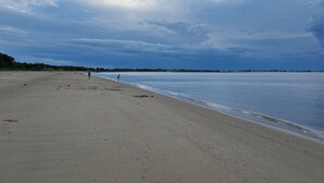 A wide sandy beach with a calm sea and a cloudy sky.