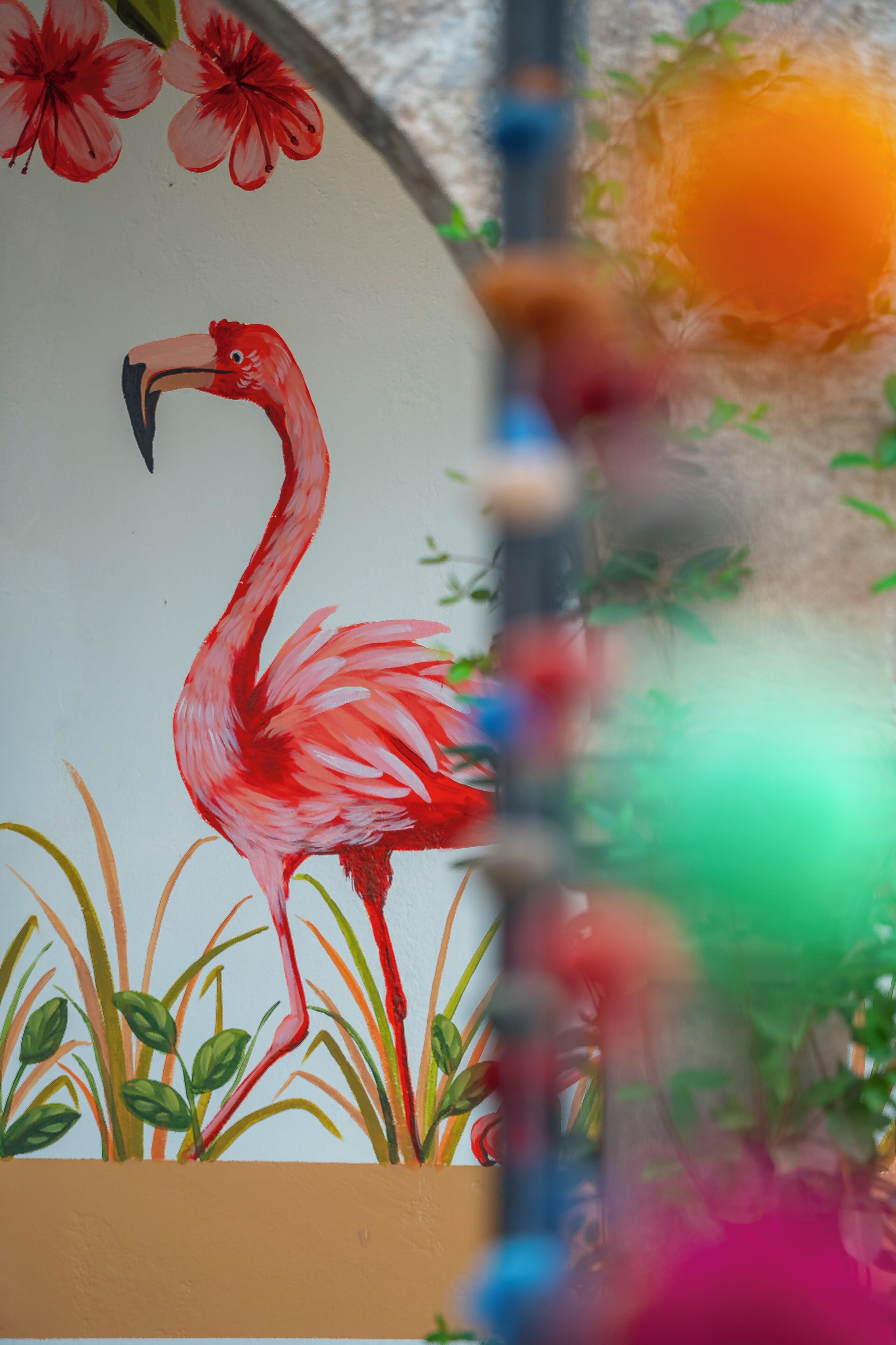 Eine Wand mit einem Gemälde von einem Flamingo inmitten von Grünpflanzen.