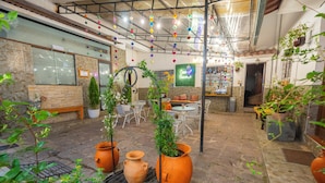 An indoor courtyard with stone flooring, terracotta pots, potted plants, and a seating area with tables and chairs.