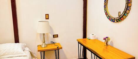 A bedroom with a bed, a bedside table with a lamp, a mirror, and a small table with a vase of flowers.