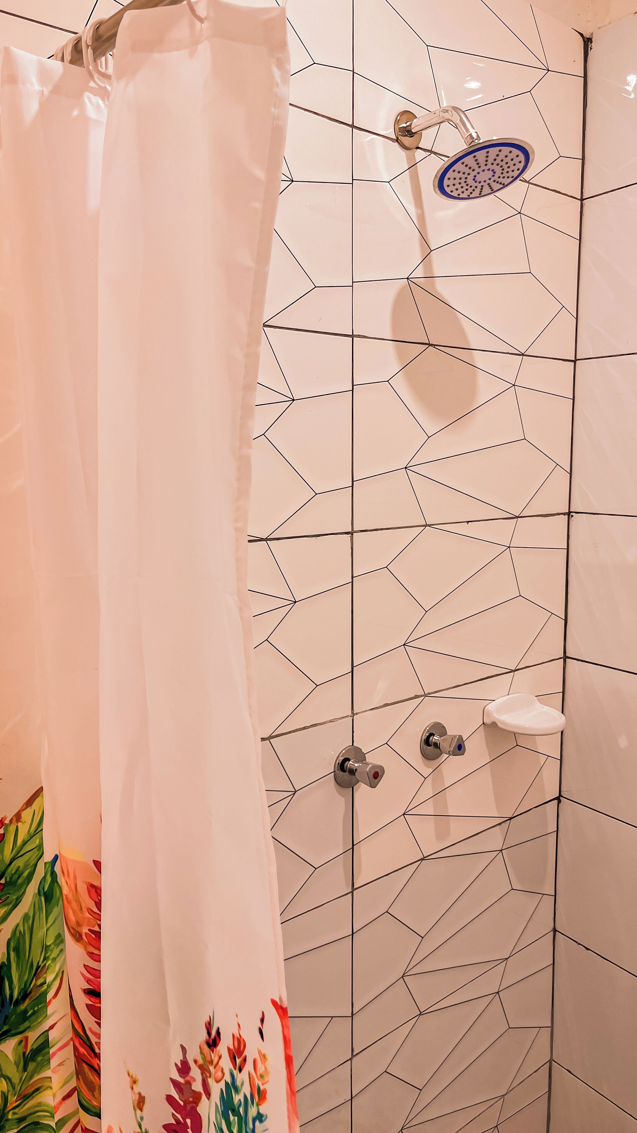 Un espace douche avec un carrelage aux motifs géométriques, une pomme de douche et un petit lavabo.
