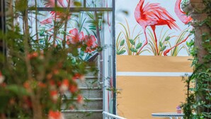 An outdoor seating area with a glass door leading to a space decorated with a flamingo mural.