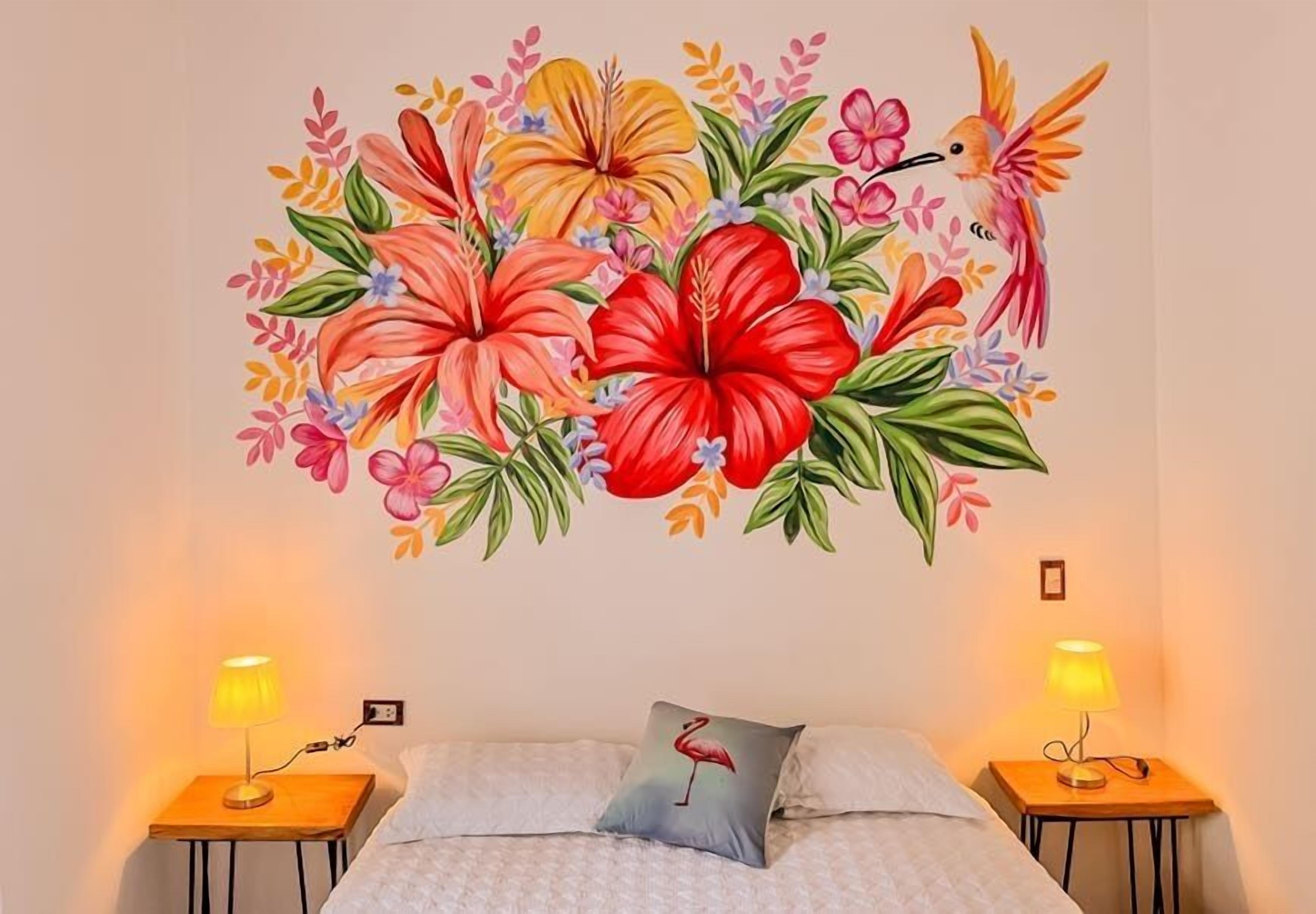 Une chambre à coucher avec une fresque florale sur le mur, deux lampes de chevet et un lit avec des oreillers.