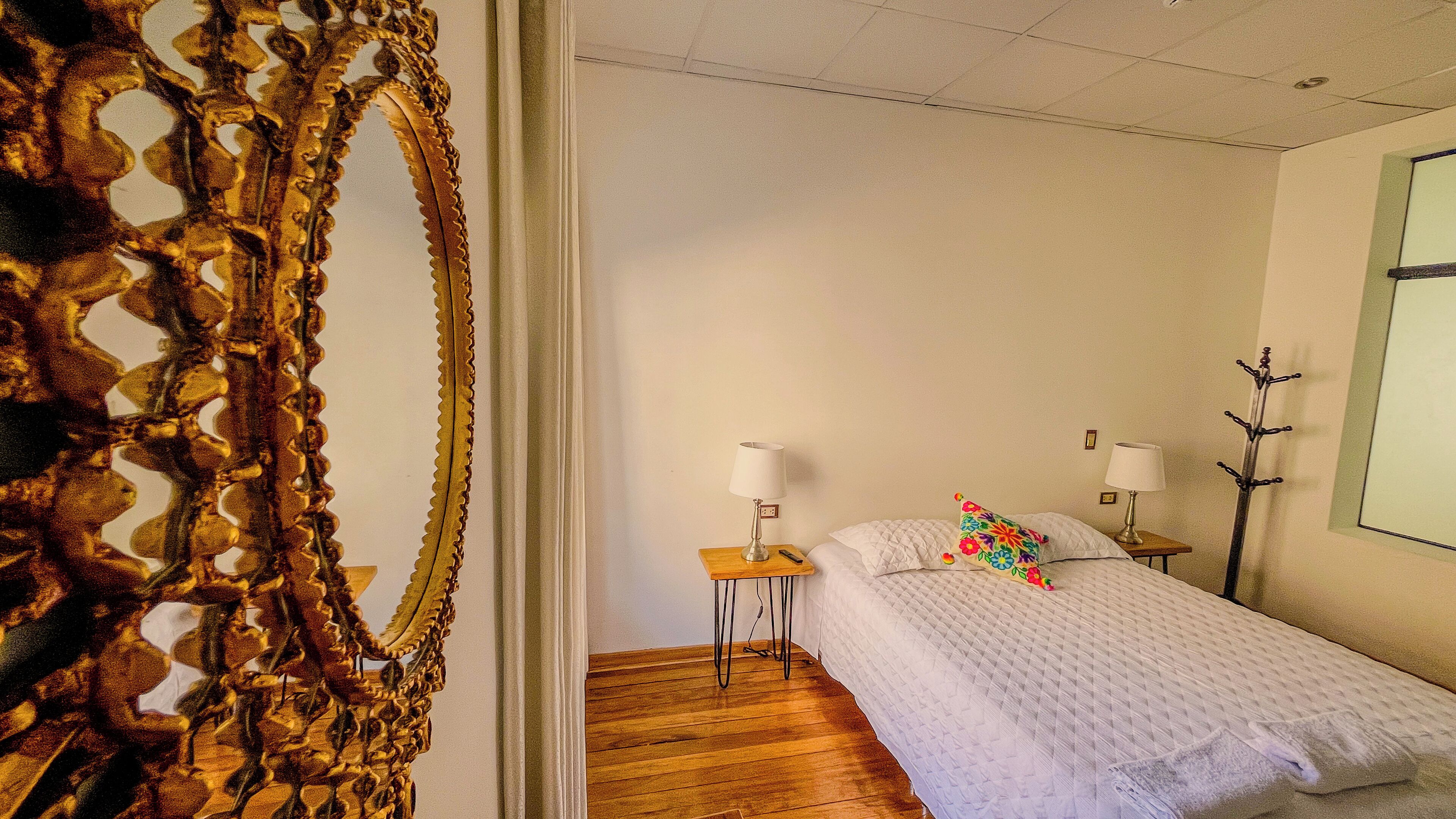 A bedroom with a bed, a nightstand, a lamp, and a coat rack.
