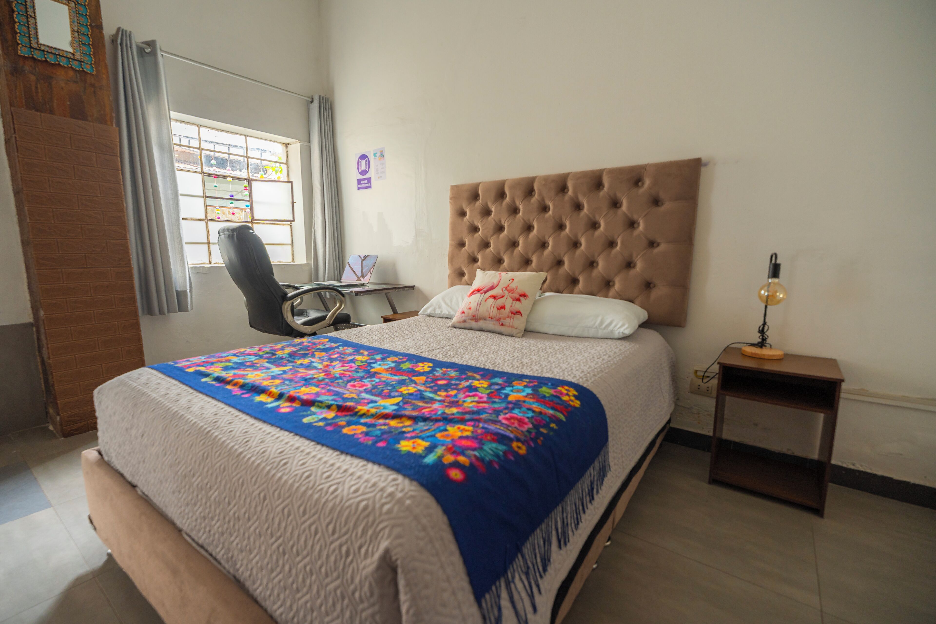 A bedroom with a large bed, a chair, a nightstand, and a window with curtains.