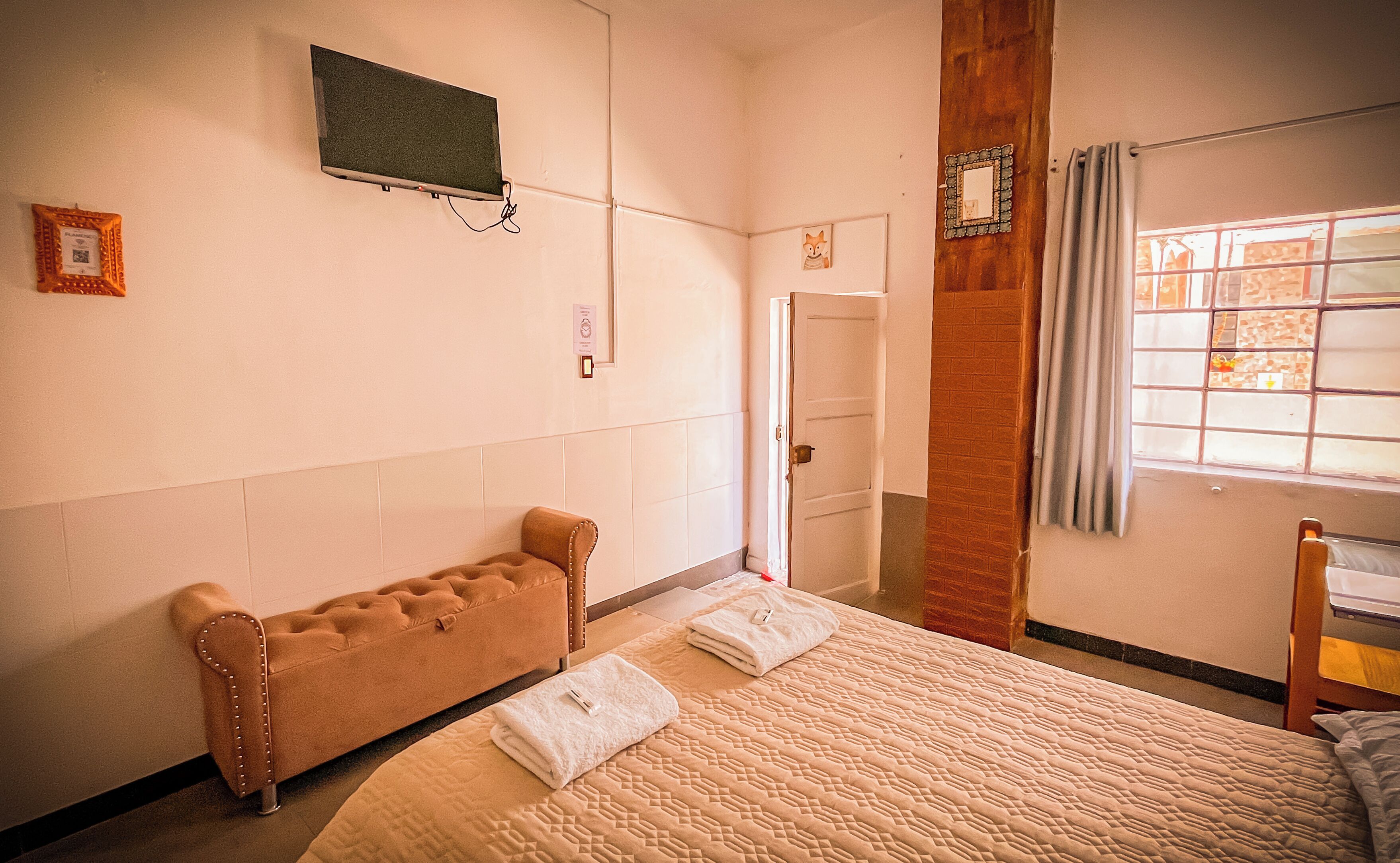 Un dormitorio con cama, una banca, una ventana con cortinas y una puerta.