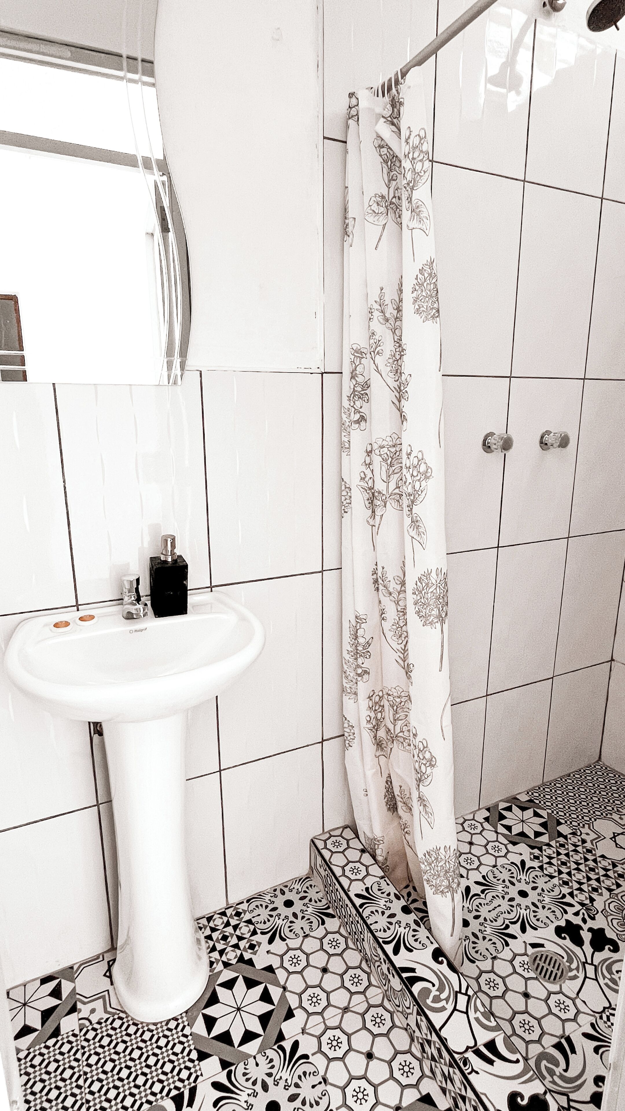 A bathroom with a white pedestal sink, a shower with a floral curtain, and patterned floor tiles.