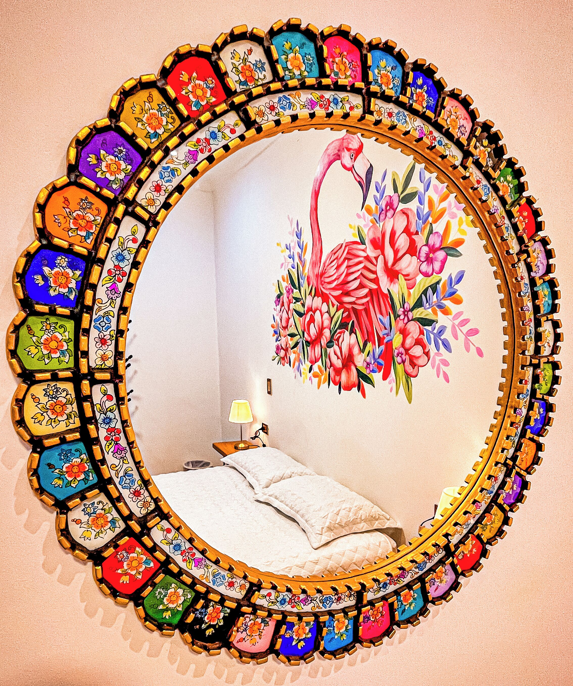 A room with a bed, a nightstand, and a mirror with a colorful floral frame.
