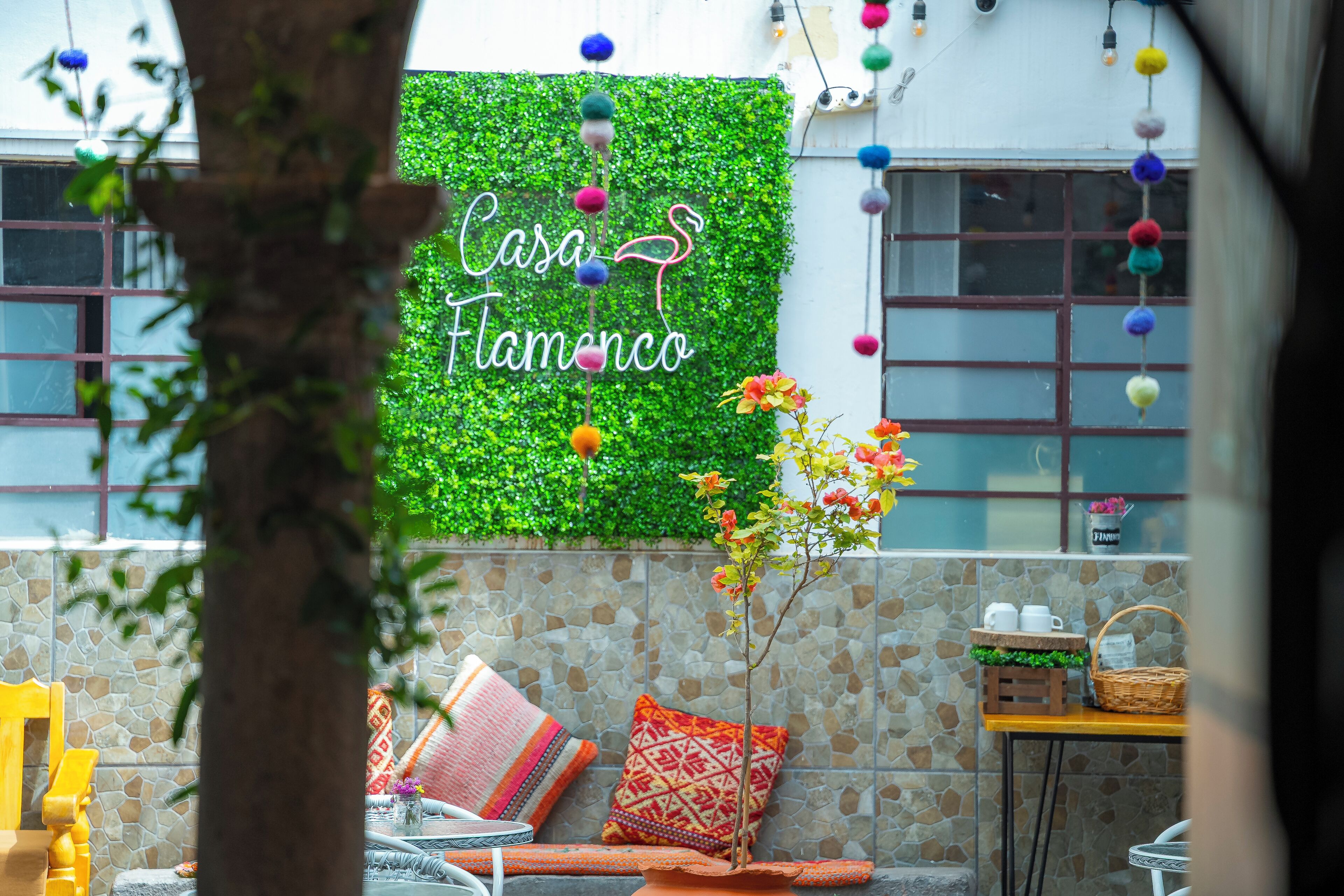 A patio area with a green wall, a sign reading "Casa Flamenco," and outdoor seating with cushions and a table.