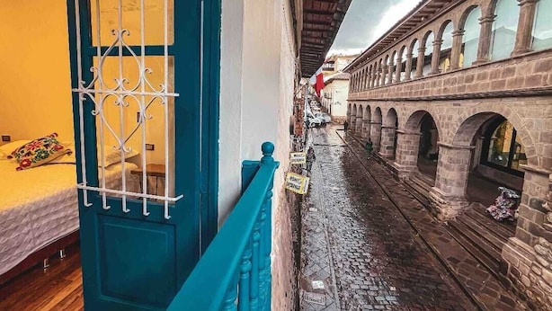 A narrow alleyway with a blue door and metal bars, leading to a building with stone arches and a tiled floor.