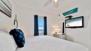 A hotel room with a bed, a ceiling fan, a TV, a window with curtains, and a sign on the wall. - GULF VIEW, POOLS, HOT TUBS, BEACH ACCESS! (Gulf Shores)