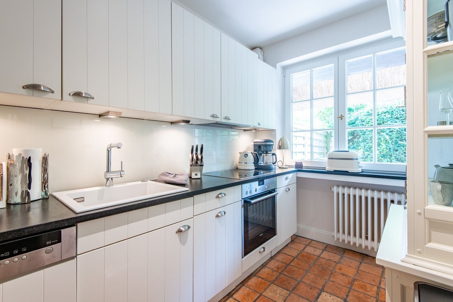 A modern kitchen with white cabinets, a black countertop, a built-in oven, and a window with a view of greenery.