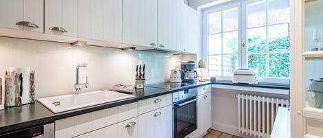 A modern kitchen with white cabinets, a black countertop, a built-in oven, and a window with a view of greenery.