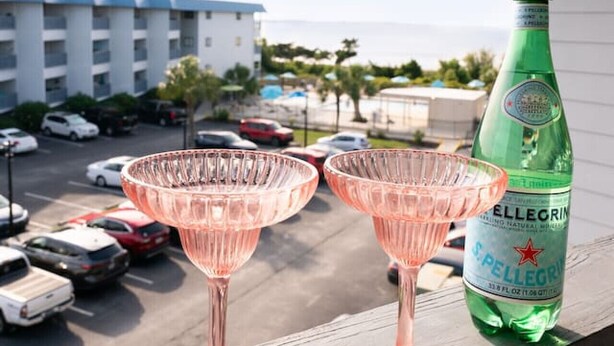 Twee roze cocktailglazen op een balkon met een fles Pellegrino water.