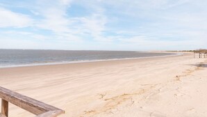 Een zandstrand met een houten looppad naar het water.