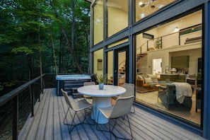 A modern outdoor deck with a hot tub, dining table, and chairs. - Uckor's Edge | Hocking Hills, Modern Cozy Cabin (Rockbridge)