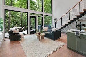 Una sala de estar moderna con ventanas amplias, una escalera y una zona de cocina.