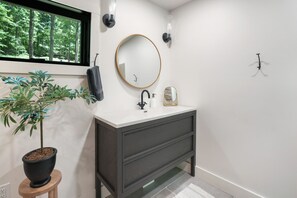 A bathroom with a dark wooden vanity, a round mirror, a potted plant, and a window with a view of trees.