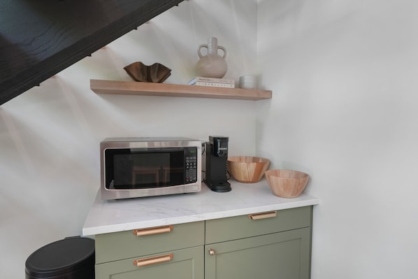 Una cocina con microondas, cafetera y cuencos de madera sobre la encimera.