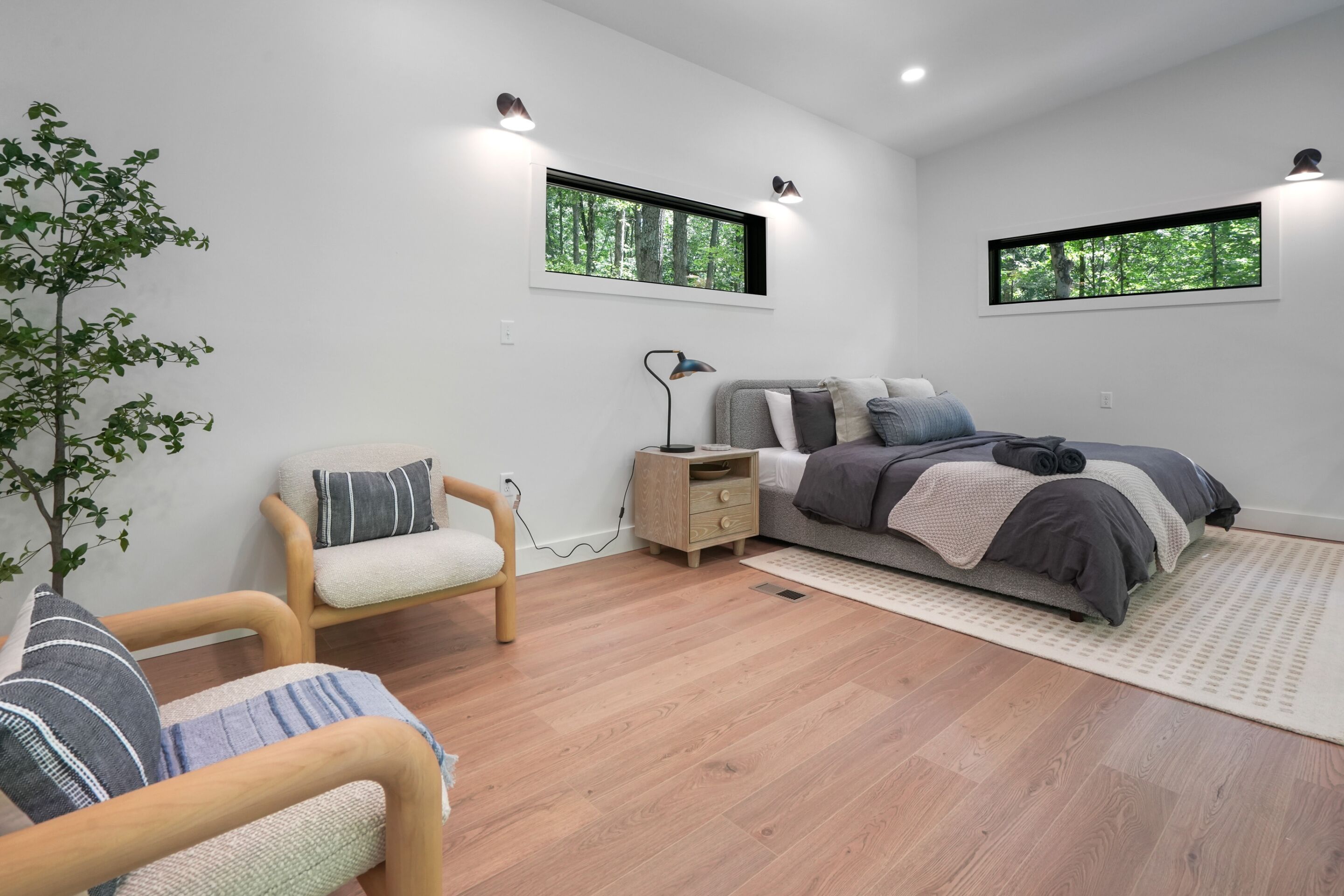 Ein modernes Schlafzimmer mit Bett, Stuhl, Nachttisch und Fenster mit Blick auf Bäume.
