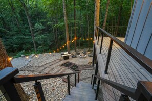 A wooden deck with a fire pit and outdoor seating, surrounded by a forested area.