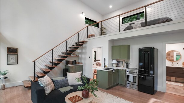 A modern apartment with a staircase, a living room with a sofa and coffee table, a kitchen with a refrigerator and stove, and a small balcony with plants. - Uckor's Edge | Hocking Hills, Modern Cozy Cabin (Rockbridge)