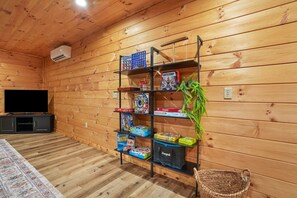 A wooden-paneled room with a television, shelves with board games, and a plant. - Rest Easy | Hocking Hills, Modern Cabin, Hot Tub (McArthur)