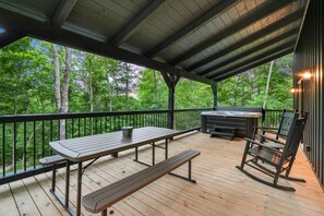 A covered outdoor deck with a picnic table, benches, a grill, and a rocking chair.