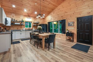 A wooden cabin interior with a kitchen, dining area, and a black door.