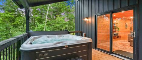 Een hottub op een houten terras met uitzicht op een bos en een gebouw met een glazen deur.