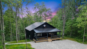 Une cabane dotée d’une véranda, entourée d’une forêt.