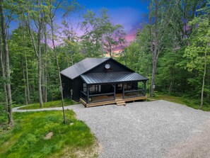 A cabin with a porch, surrounded by a forest. - Rest Easy | Hocking Hills, Modern Cabin, Hot Tub (McArthur)