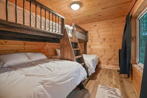 Une cabine équipée de deux lits superposés, d’un plafond en bois, d’une fenêtre et d’une échelle.