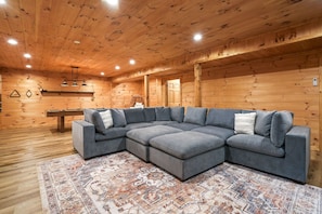 A log cabin interior with a sectional sofa, wooden walls, and a patterned rug.