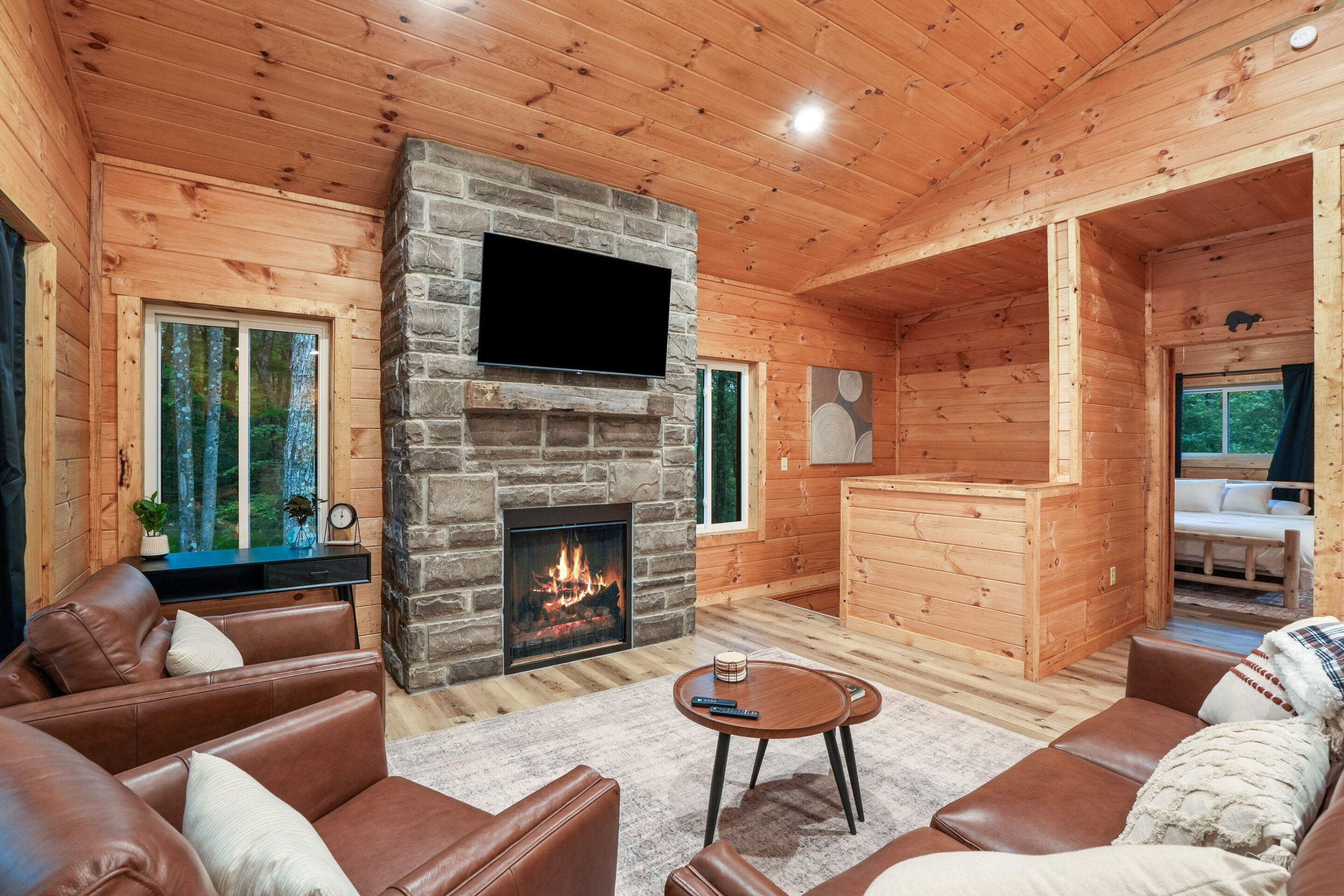 Interior acogedor de una cabaña con chimenea de piedra, sofás de cuero, televisor de pantalla plana y comedor de madera.