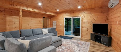 A cozy cabin interior with a sectional sofa, a flat-screen TV, and a wooden ceiling.