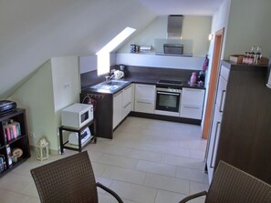 A compact kitchen with a microwave, oven, and sink. There is a small dining area with chairs.