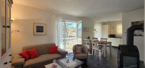Una sala de estar con sofá, sillón y mesa de comedor. Hay una chimenea y vistas al exterior.