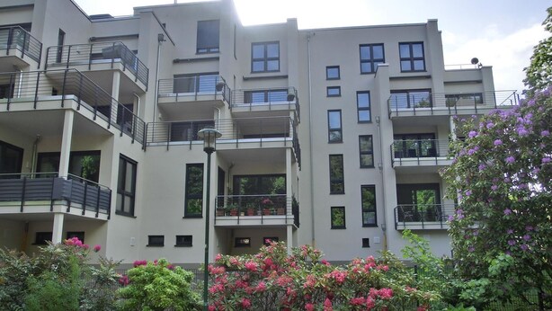A modern multi-story residential building with balconies, a garden area with flowering plants, and a street lamp. - Ferienwohnung Lp24 - Strandnahe 2-zi.-fewo für 2 Pers.- im 4. OG in Ruhiger Lage (Graal-Müritz)