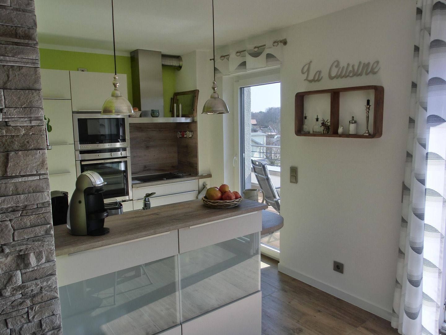 A modern kitchen with a stone accent wall, a built-in oven, and a wooden countertop.