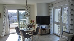 A modern living room with a dining area, a flat-screen TV, and large windows. - Ferienwohnung Lp24 - Strandnahe 2-zi.-fewo für 2 Pers.- im 4. OG in Ruhiger Lage (Graal-Müritz)