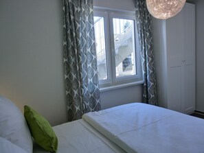 Un dormitorio con cama, ventana y cortinas.