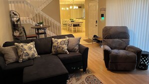 A living room with a sectional sofa, a recliner, a staircase, and a dining area in the background.