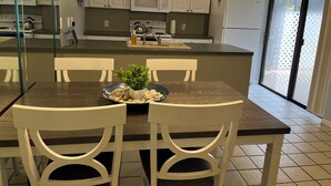 A modern kitchen with white cabinets, a microwave, a refrigerator, and a dining area with a table and chairs.