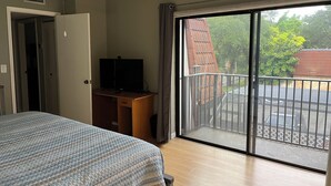 A bedroom with a bed, a desk with a TV, a ceiling fan, and a large sliding glass door to a balcony.